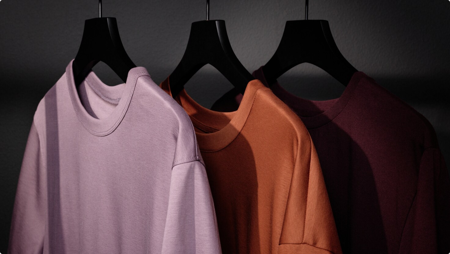 Tre färgglada t-shirts hänger på svarta galgar.