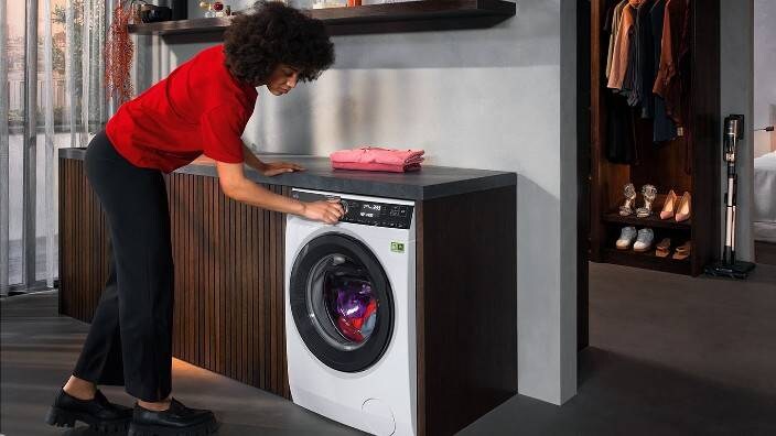 Nainen on käynnistämässä edestä täytettävää pesukonetta. 