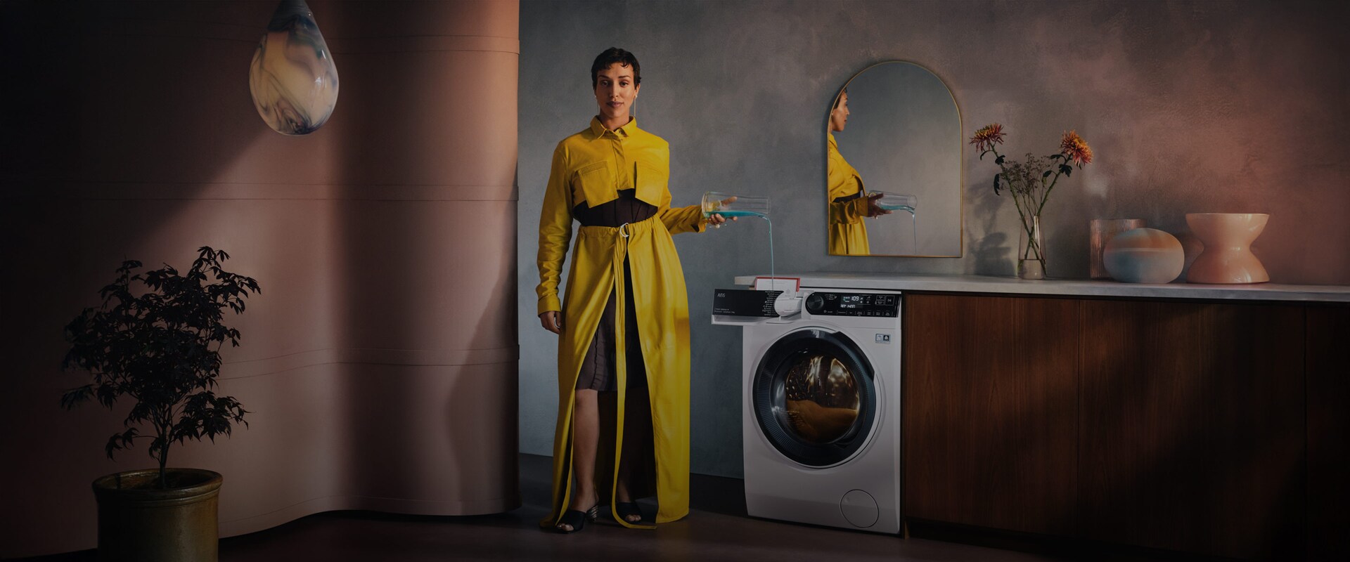 Nainen keltaisessa mekossa kaataa pesuainetta pesukoneeseen.