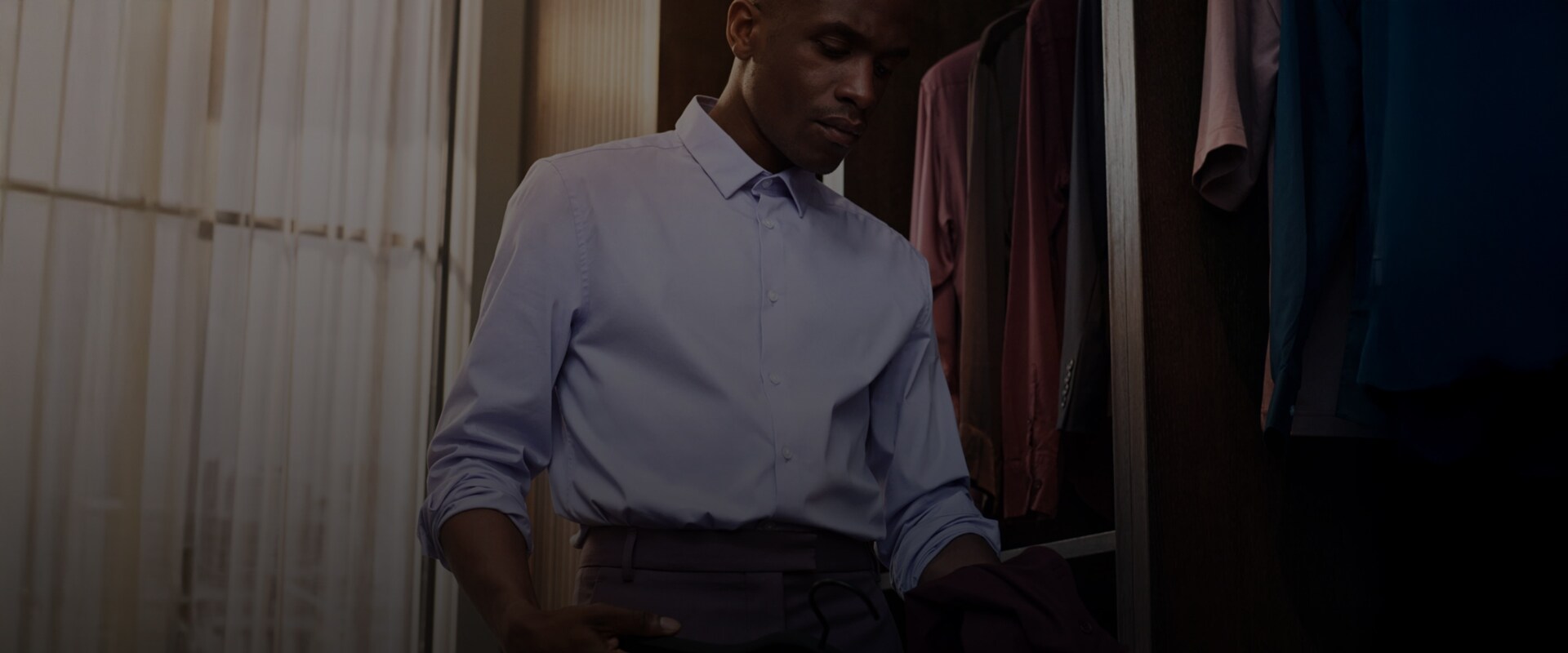 Mies sinisessä paidassa valikoi vaatteita vaatekaapista.